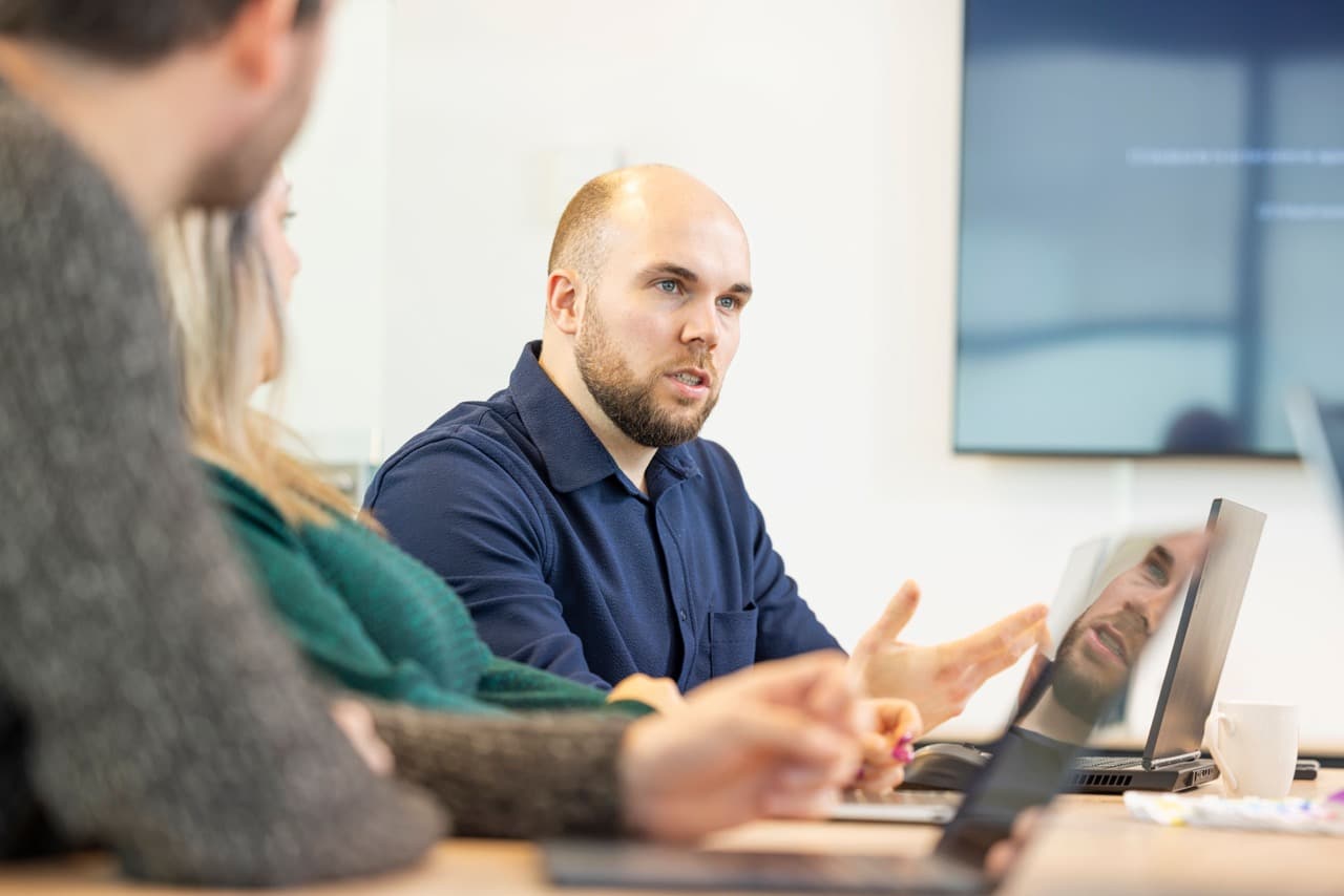 Een man in een blauwe overhemd spreekt tijdens een vergadering met collega's van Lifegoods.
