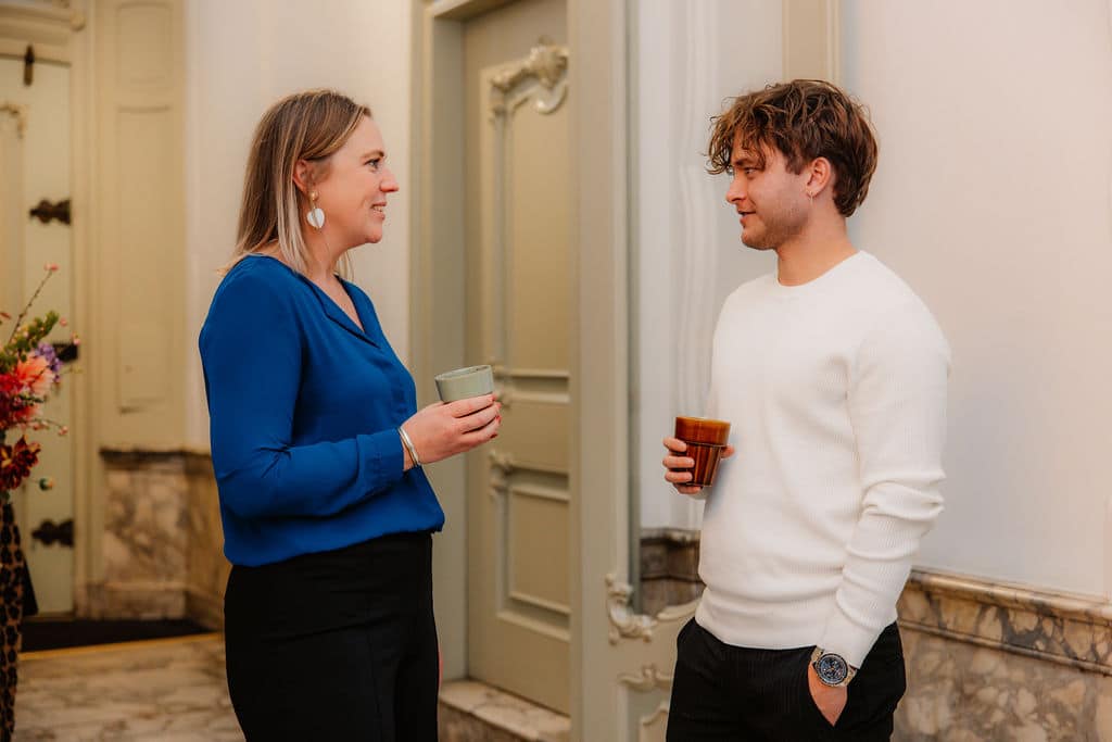Twee personen die met elkaar in gesprek zijn met allebei een beker in hun hand.